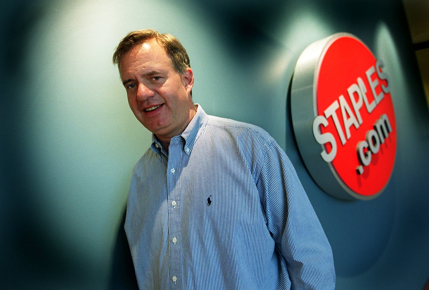 Thomas G. Stemberg standing beside a Staples.com sign in an office
