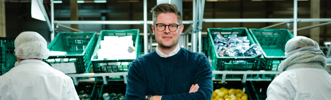Thomas Griesel standing between workers and green ingredient crates at a food-processing facility
