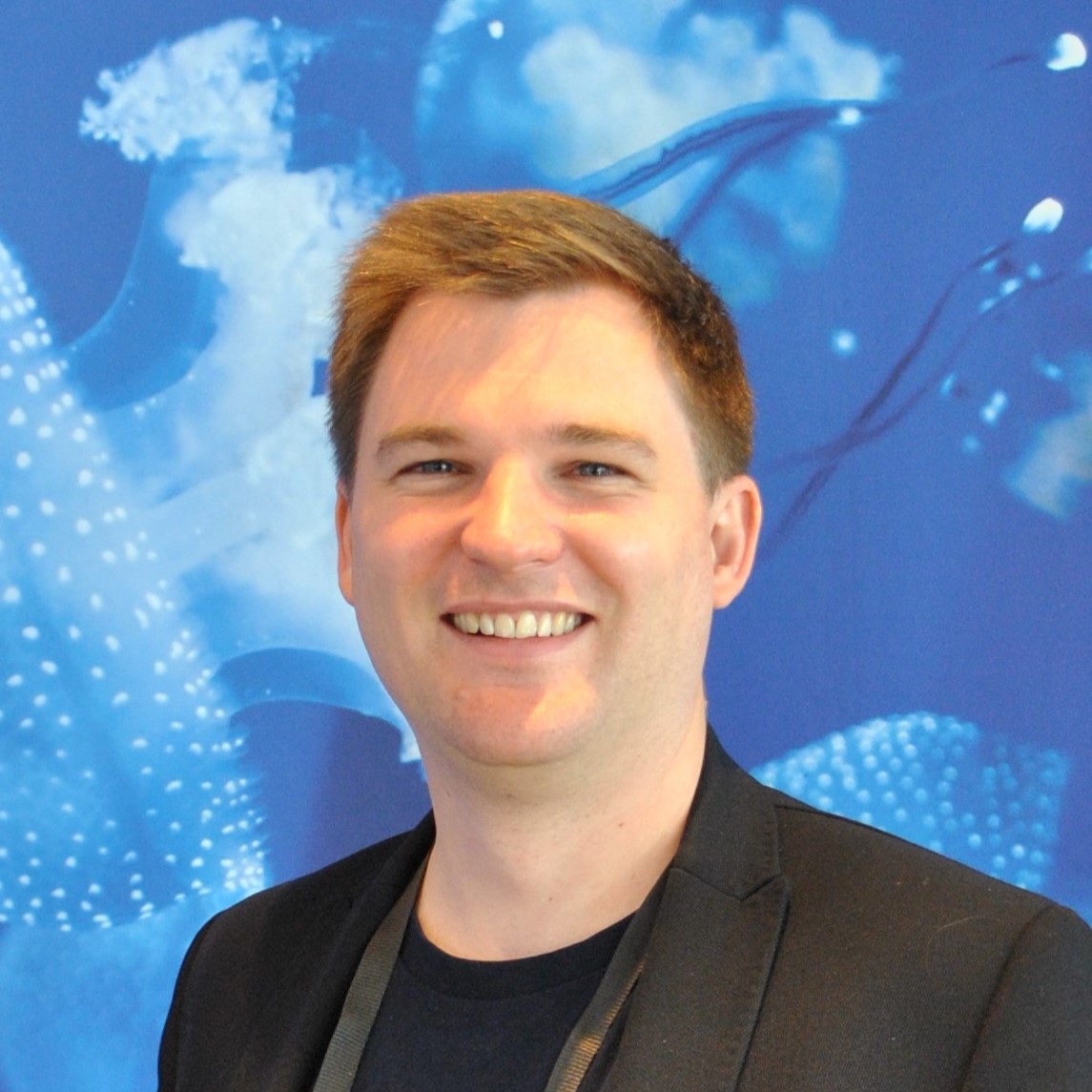 Thomas Kösters smiling in front of a blue illustrated backdrop