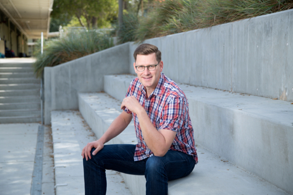 Mac Harman, wearing glasses and a checked shirt, seated on outdoor concrete steps