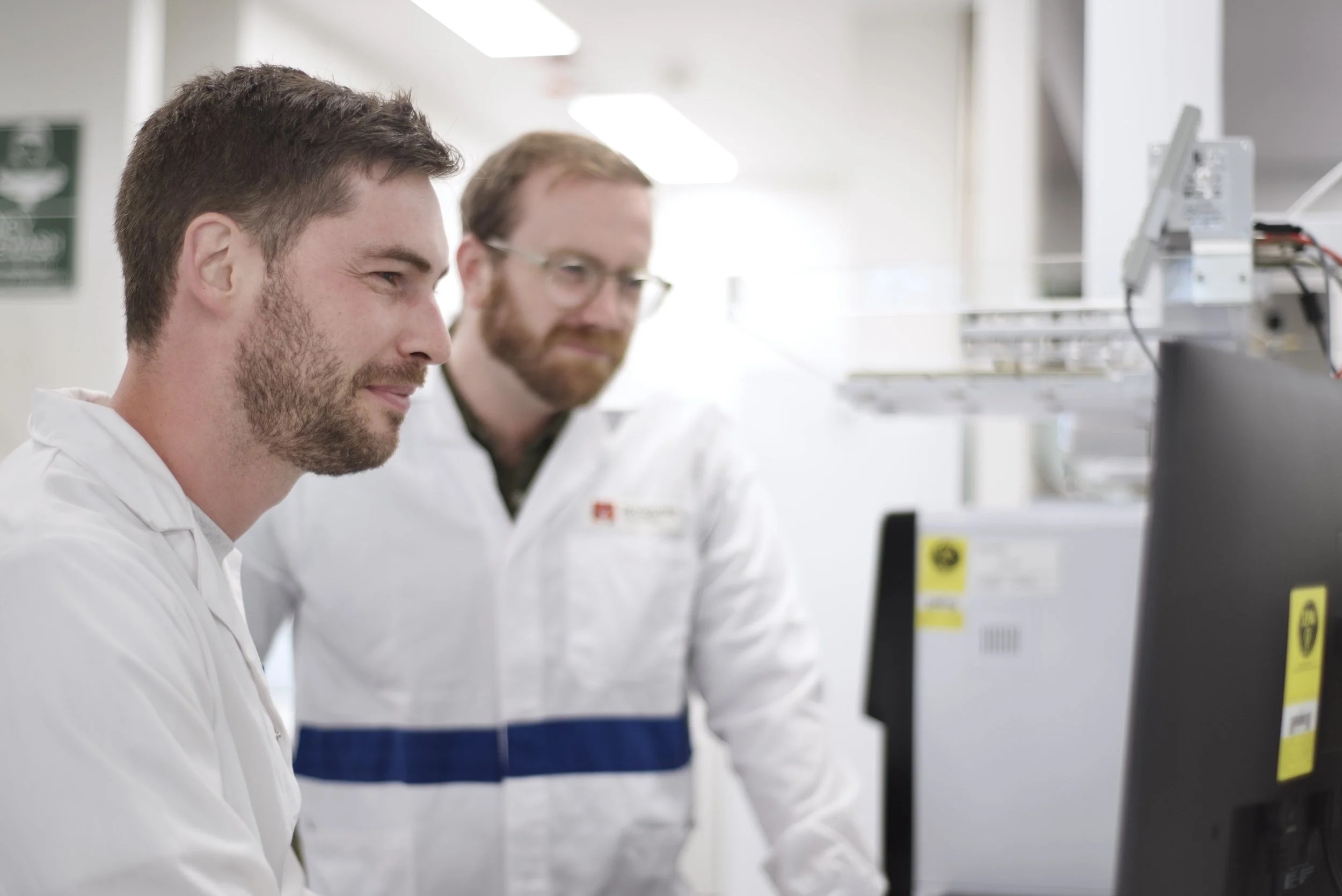 Tom Williams on the left and Alex Carpenter on the right, wearing lab coats beside laboratory equipment