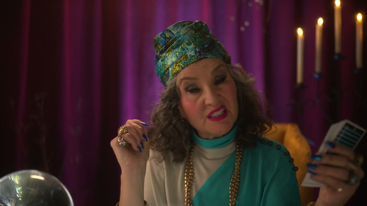 A character in a jeweled head wrap sits beside a crystal ball in PacificSource’s Cards commercial.