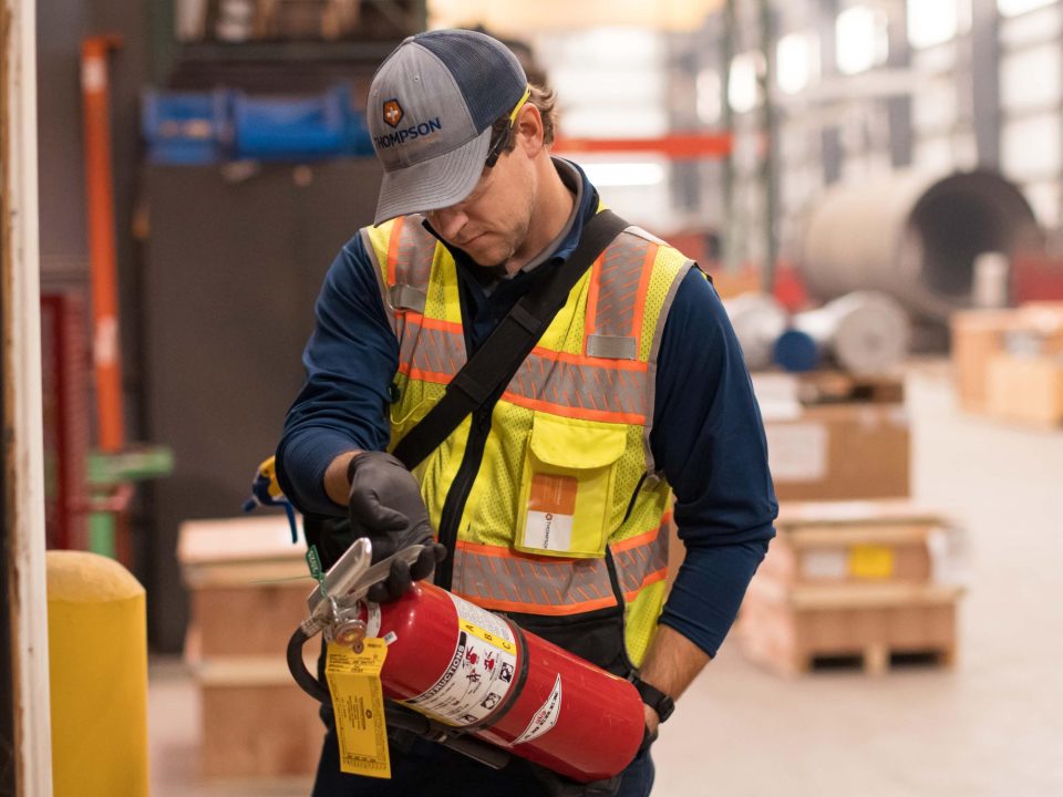 A Thompson Safety technician inspecting a red fire extinguisher