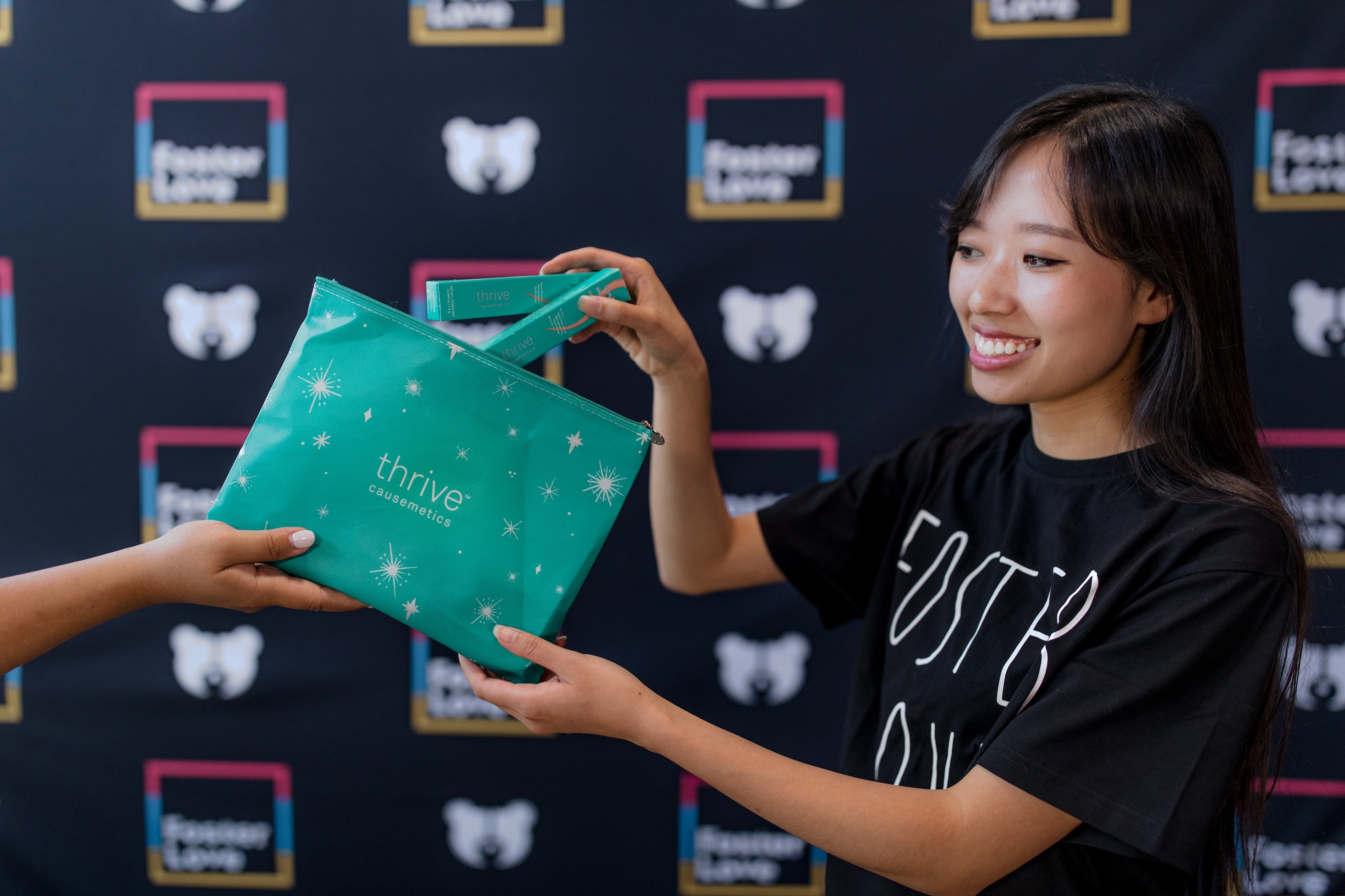 A smiling participant receives a teal cosmetics bag at a Foster Love and Thrive Causemetics event