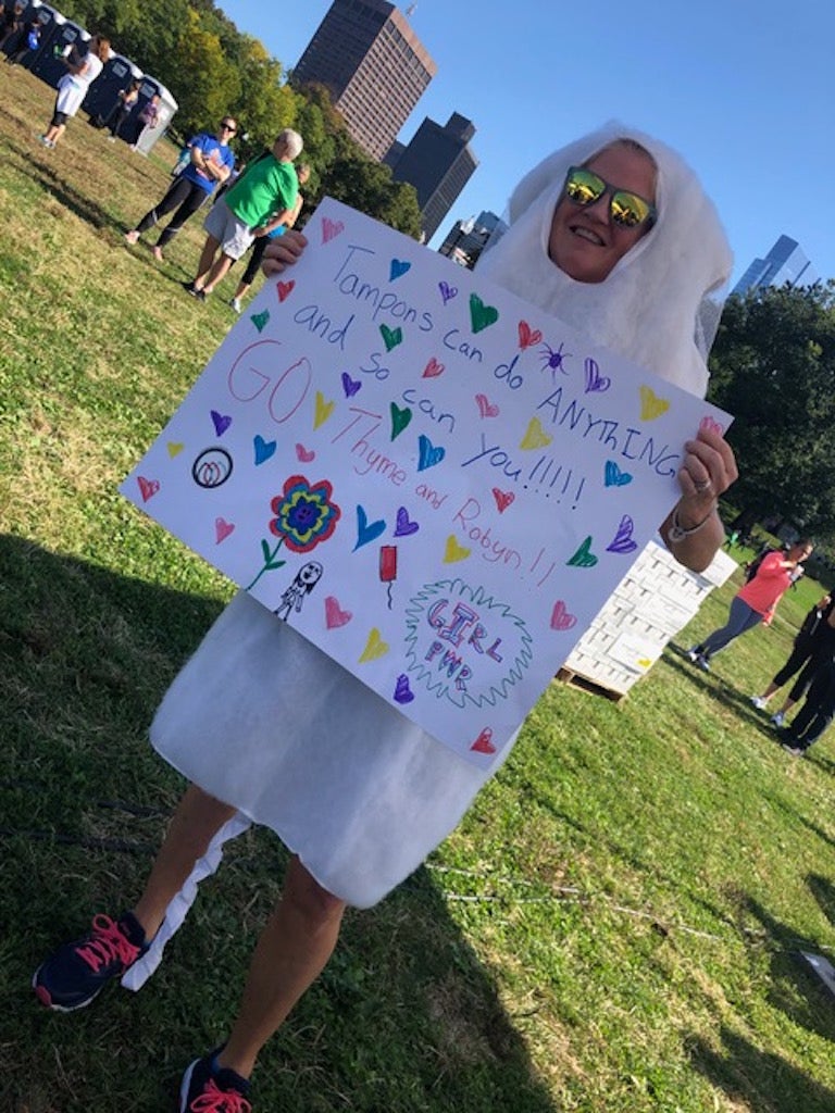Thyme Sullivan wearing a tampon costume and sunglasses, holding a handmade sign at the 2019 Boston race
