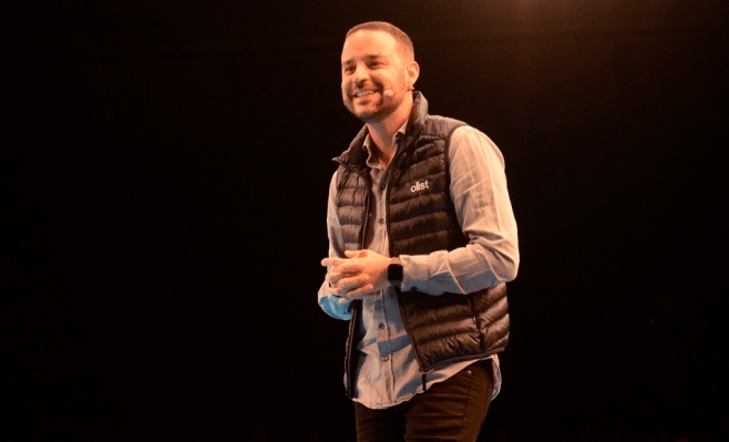 Tiago Dalvi speaking onstage, wearing an Olist vest