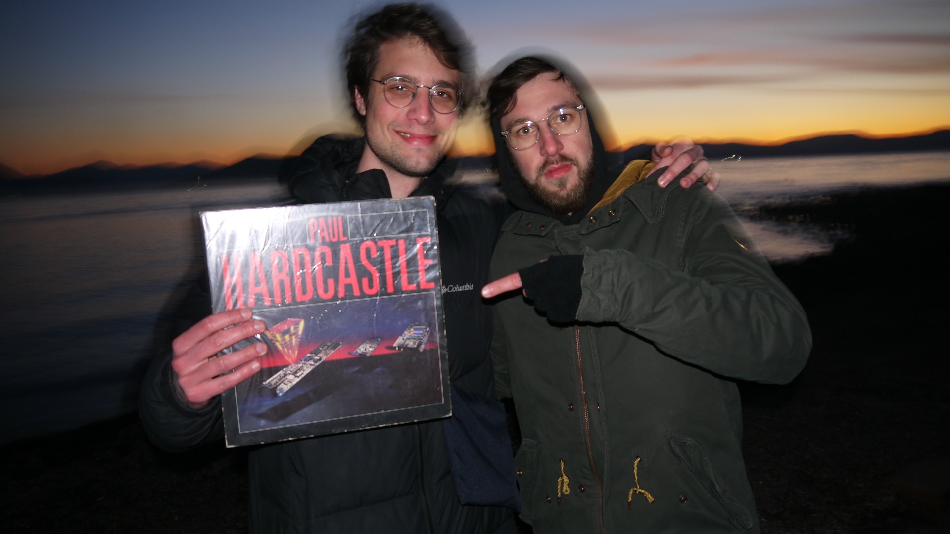 Tiago Gerstheimer, at right, posing with another person and a Paul Hardcastle record beside the water at sunset