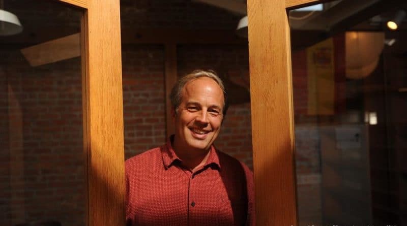 Tim Choate smiling at an office, framed by wood beams
