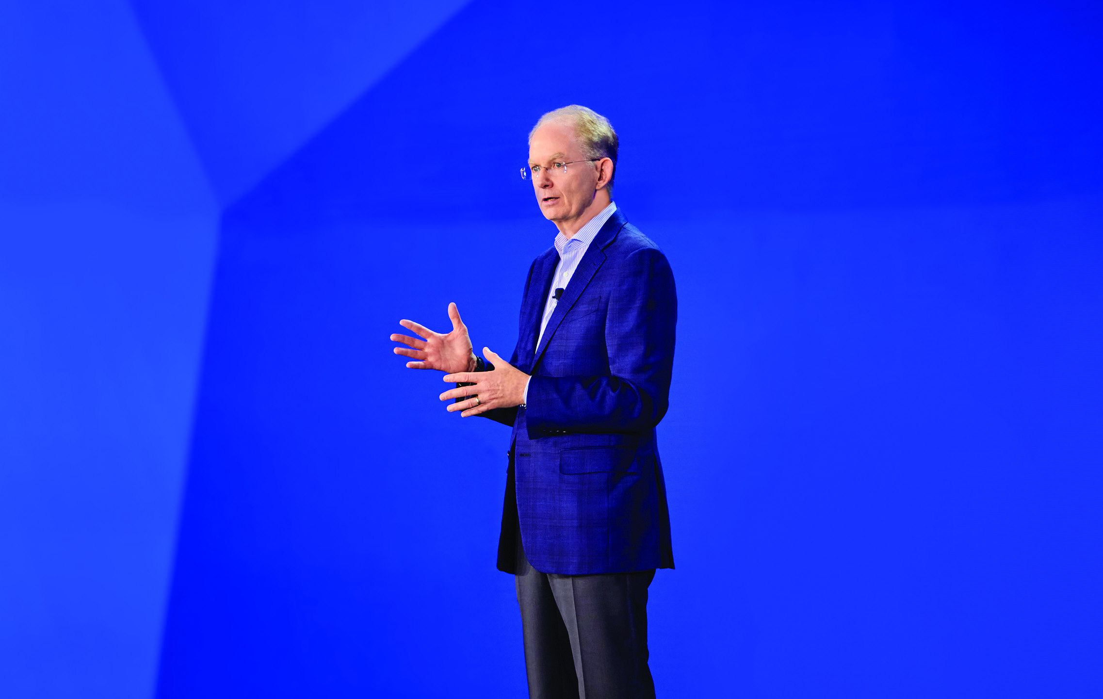 Tim Gokey speaking on a stage against a blue geometric backdrop
