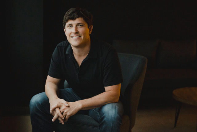Tim Heyl seated in a dark room, wearing a black polo shirt