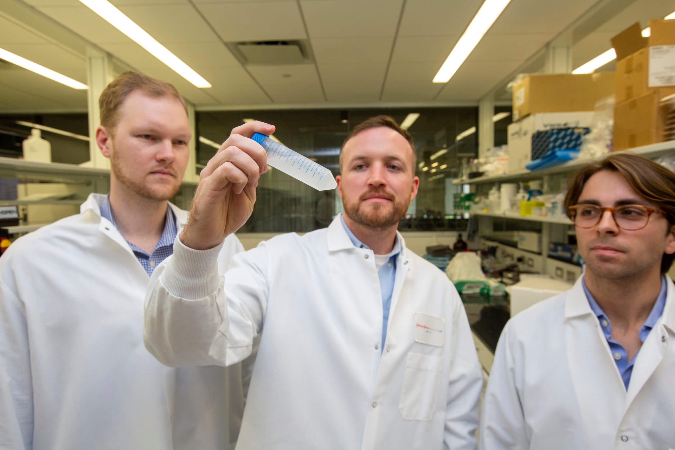 Tim Keane holds a laboratory sample tube, with two founding-team colleagues beside him.