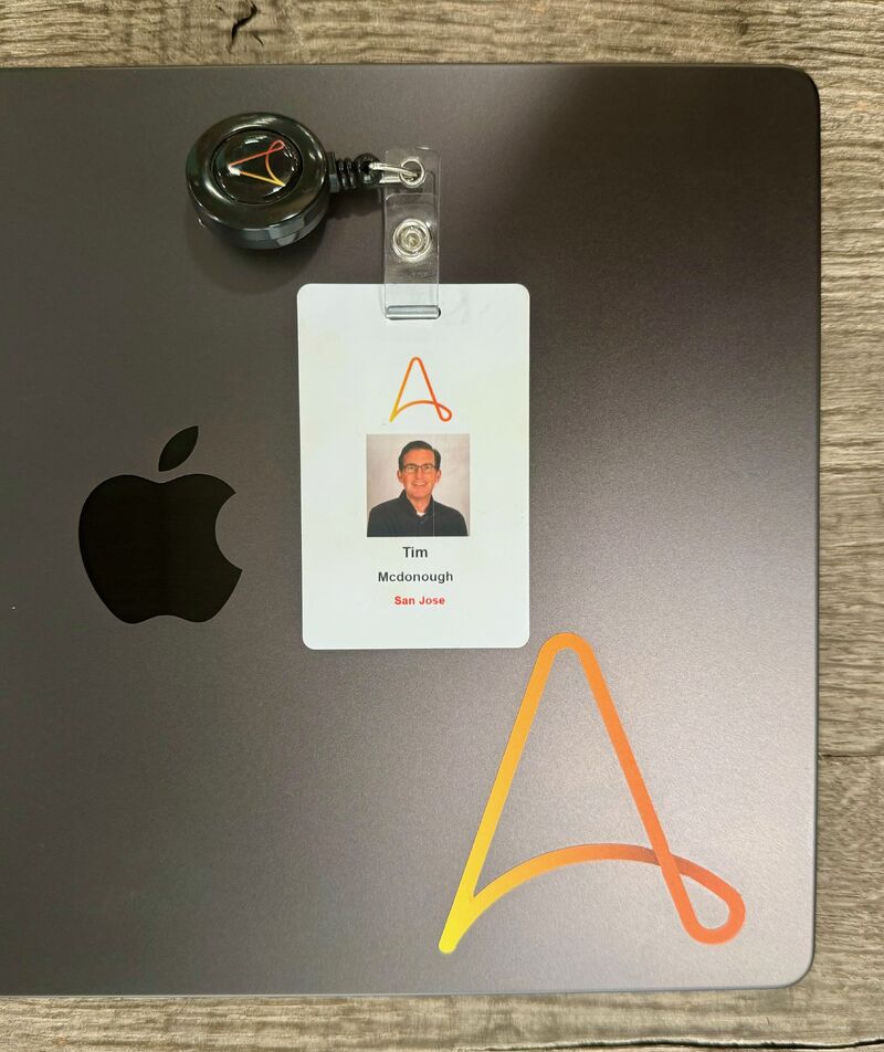 Tim McDonough's Automation Anywhere employee badge resting on a MacBook marked with the company's orange symbol