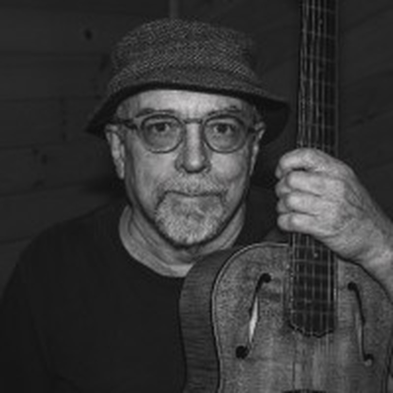 Tim Negris wearing a cap and glasses while holding a stringed instrument