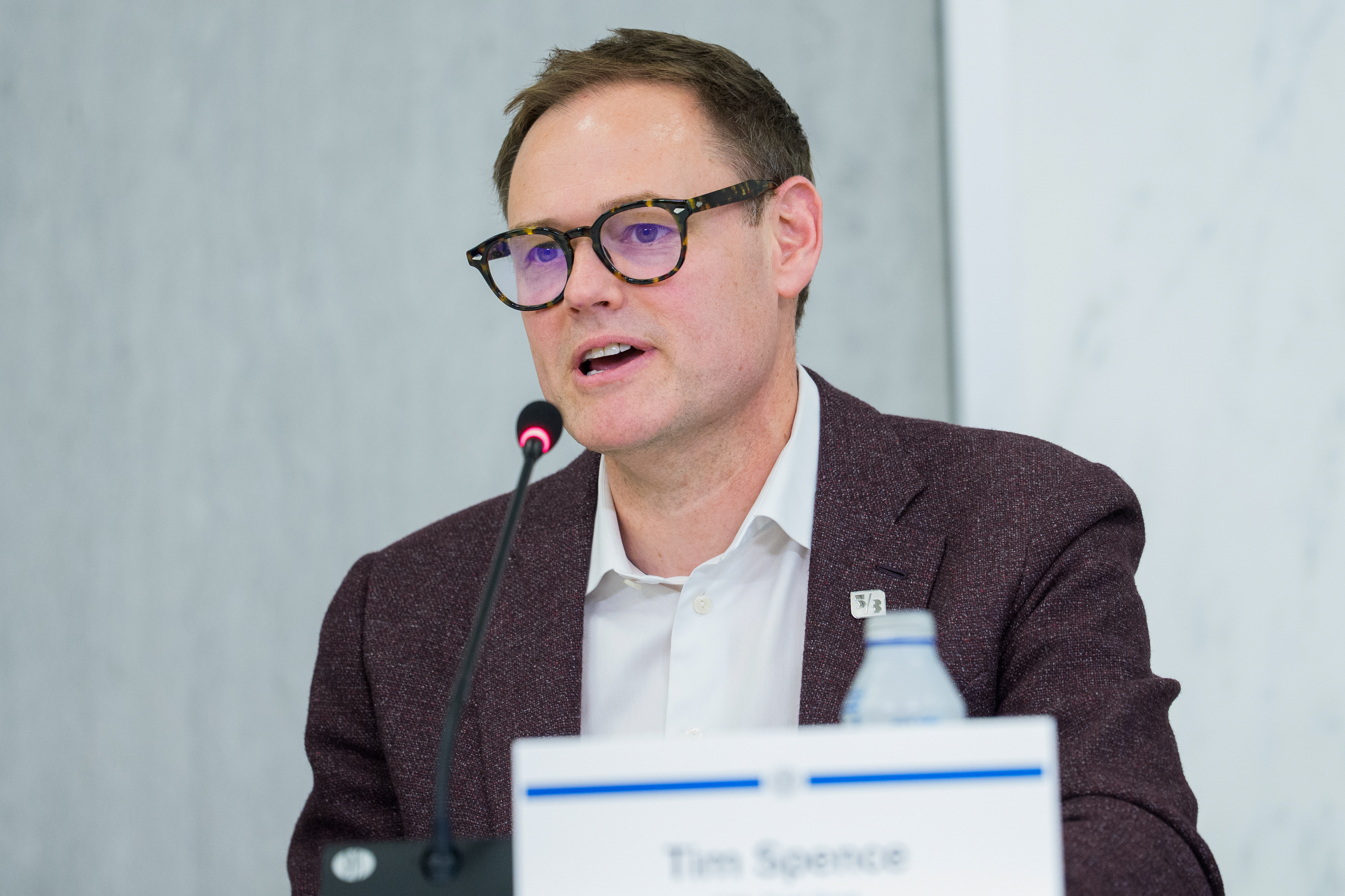 Tim Spence wearing glasses and speaking into a microphone at a public event