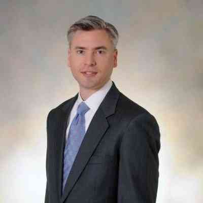 An earlier corporate portrait of Timothy Boswell, wearing a dark suit and blue tie