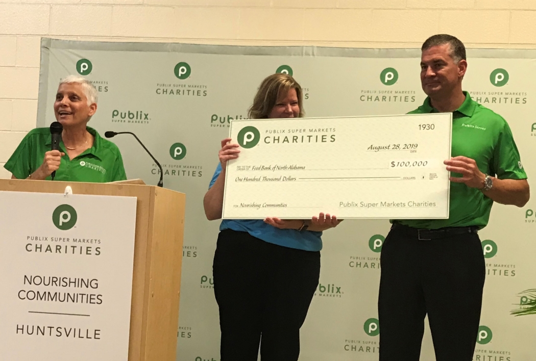 Tina Johnson speaks at left as Shirley Schofield and Kevin Murphy hold a $100,000 donation check in Huntsville.