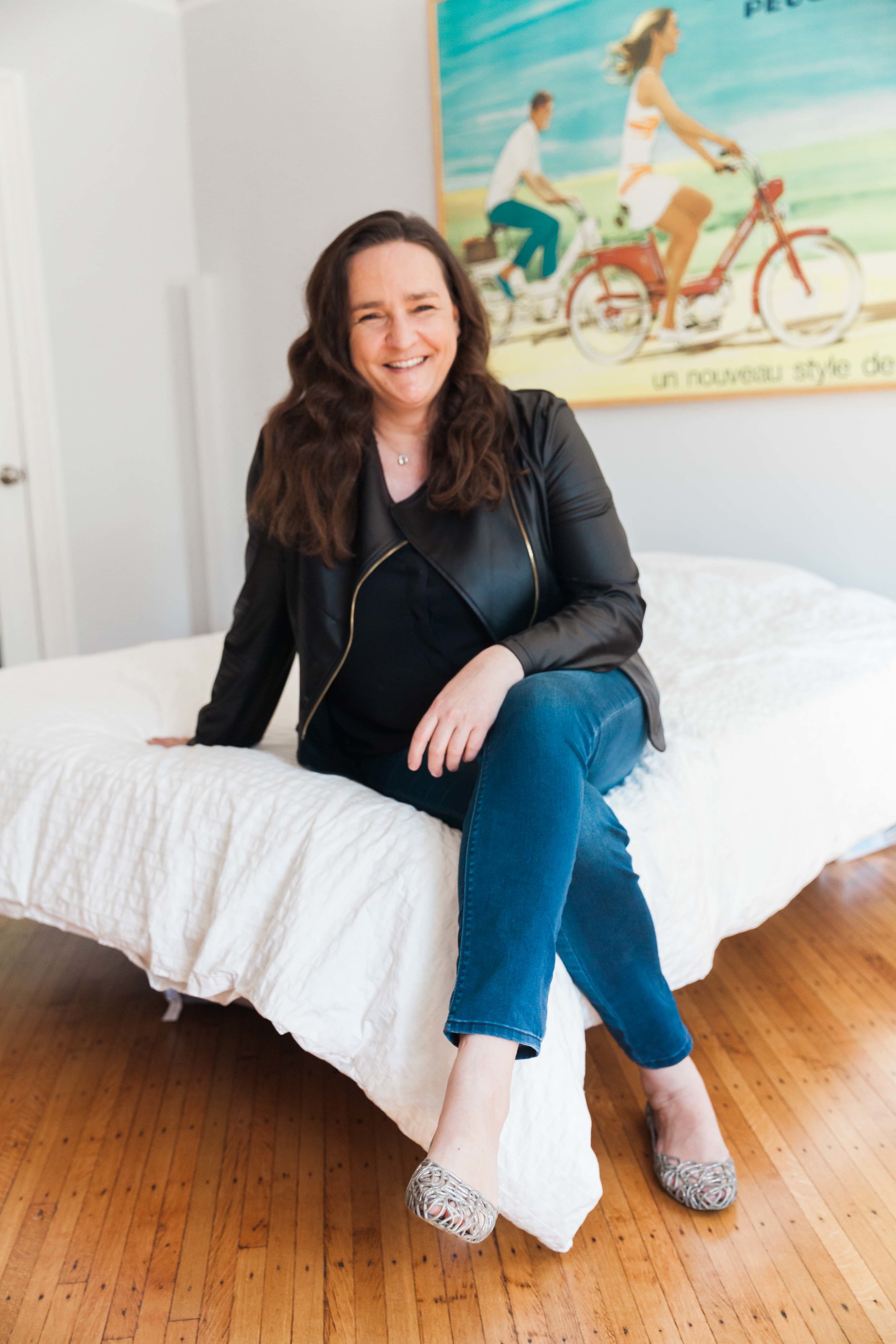 Tina Roth Eisenberg laughing while seated beneath a vintage cycling poster