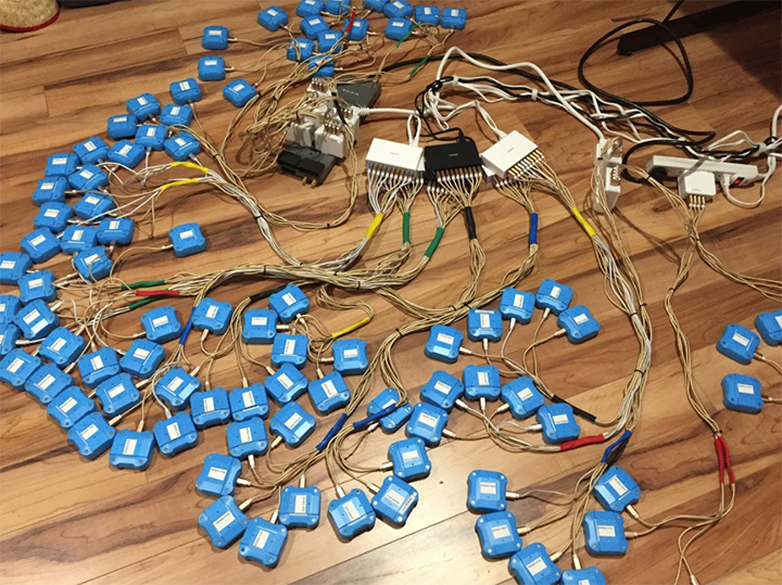 Early blue Tive trackers connected by bundles of wires on a wooden floor