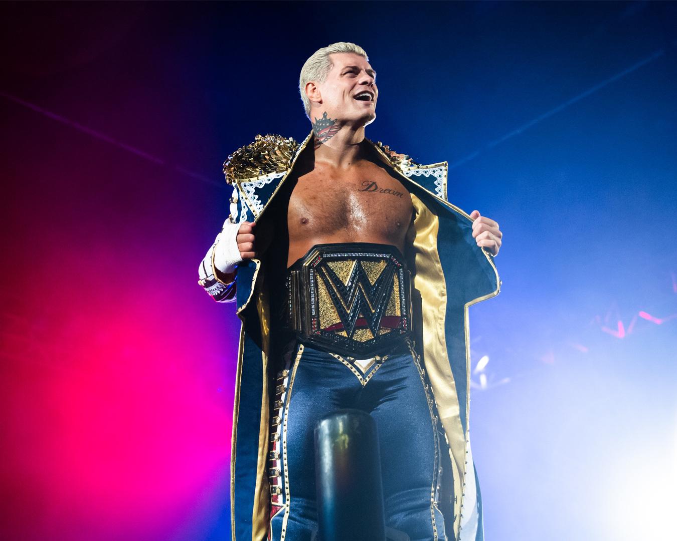 WWE performer Cody Rhodes wearing a championship belt beneath blue and pink arena lights