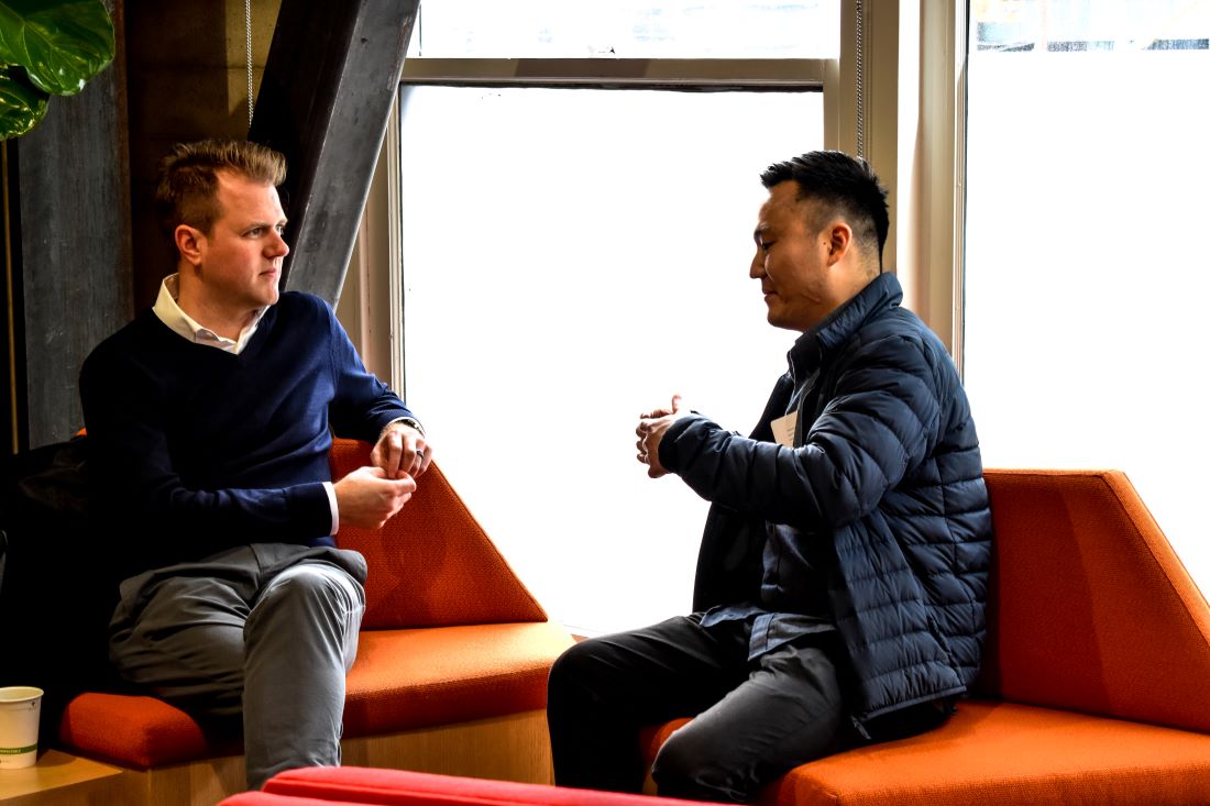 Matt Tillman, left, seated in conversation on an orange sofa