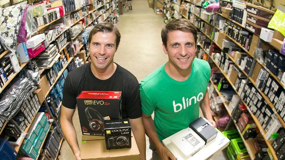 Tobin Moore and Adam Vitarello holding boxed merchandise between warehouse shelves