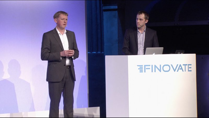 Toby Hughes speaks on the left while Dave Tonge stands at the Finovate lectern during the 2015 Moneyhub demonstration