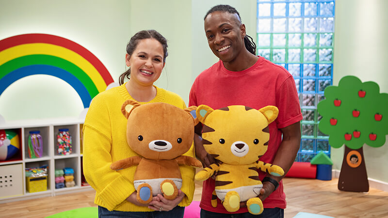 The Baby Club presenters Giovanna Fletcher and Nigel Clarke holding bear and tiger toys in a colourful studio