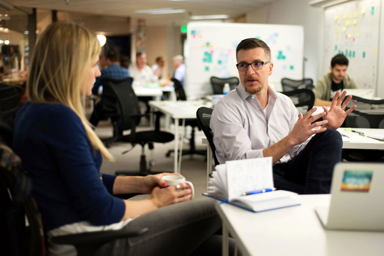 Toby Krout, seated at right, talking with a colleague in a shared workspace