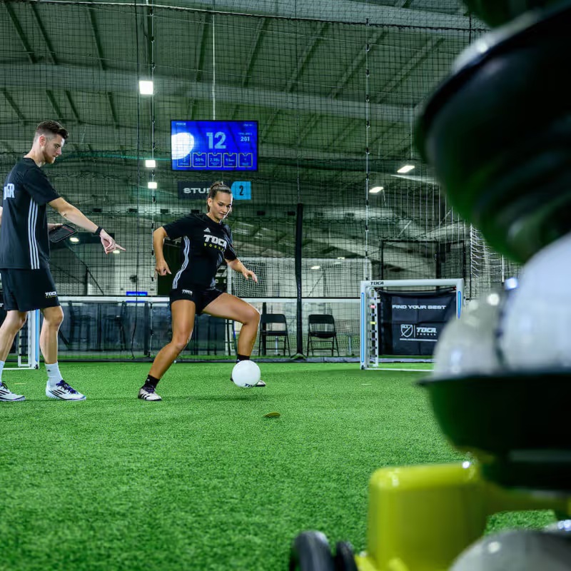 A TOCA coach works with a soccer player beside the Touch Trainer on indoor turf