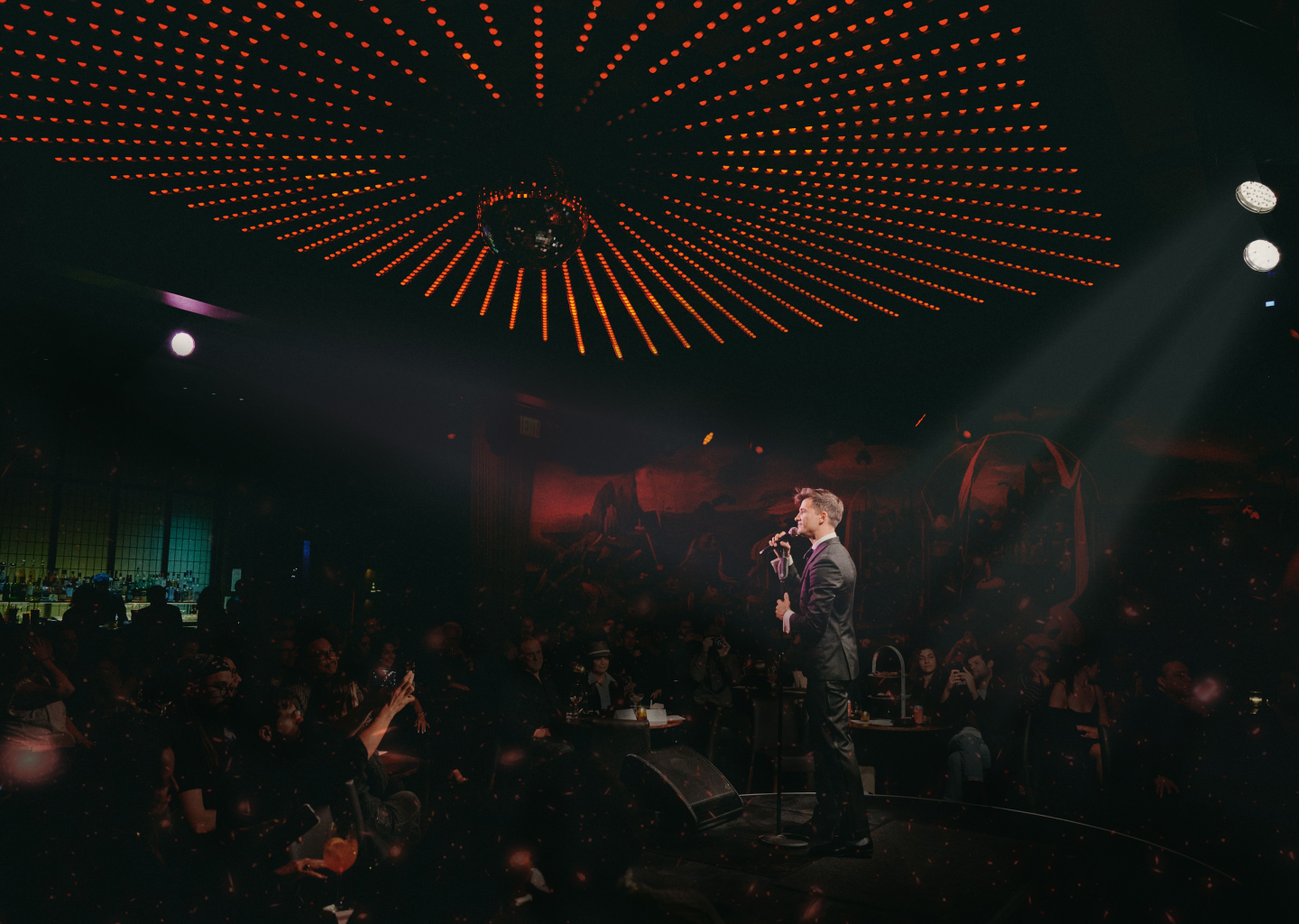 A performer sings to an audience beneath a circular canopy of lights