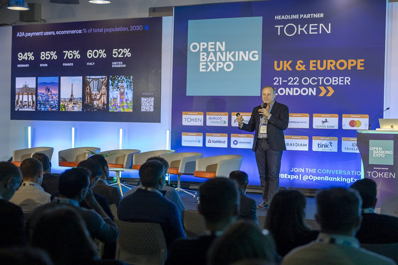 Todd Clyde holding a microphone while presenting on stage at Open Banking Expo UK and Europe 2025