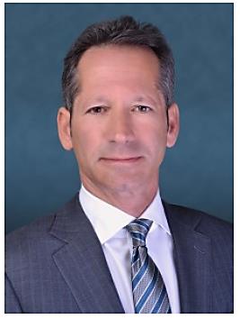 Historical press portrait of Todd Schuster wearing a suit and patterned tie