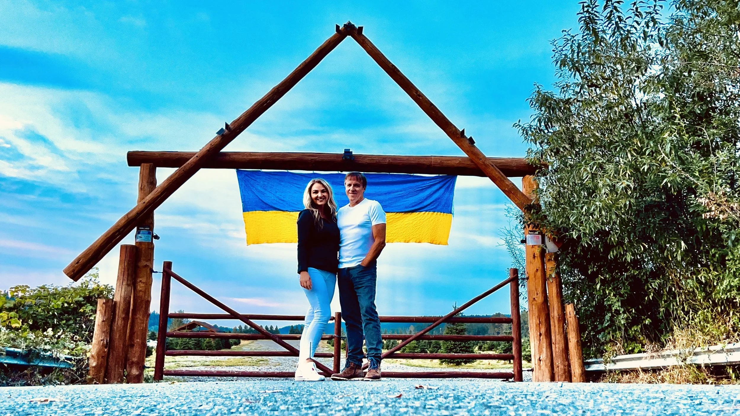 Yelena and Tom Button standing at the entrance to Buttonwood Farm beneath a Ukrainian flag