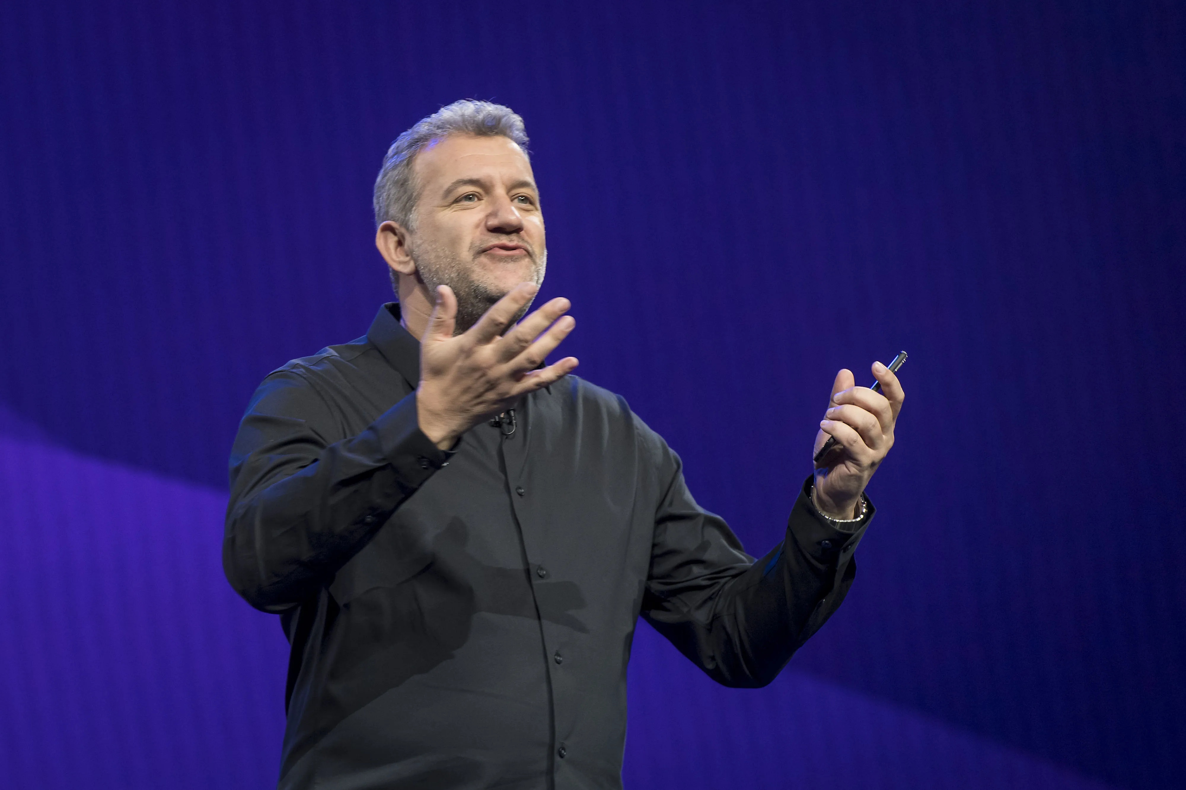 Tom Conrad speaking onstage, gesturing while holding a presentation remote