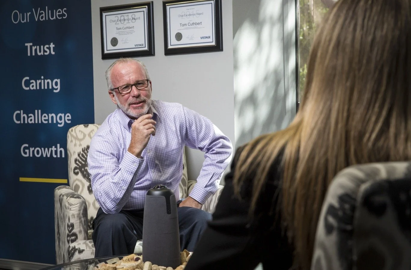 Tom Cuthbert seated in conversation, with Trust, Caring, Challenge and Growth displayed behind him