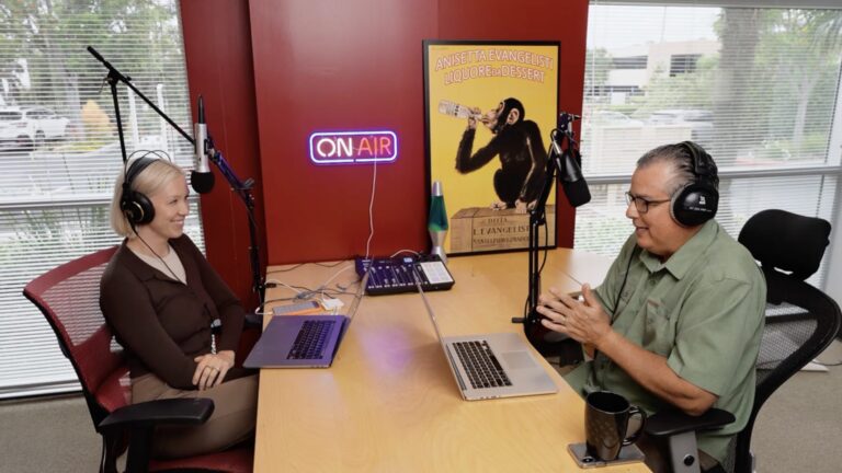 Kate Houser and Tom Gallego wearing headphones and recording across an office table