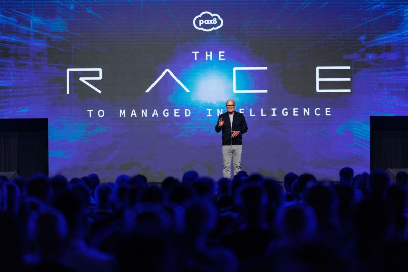 A speaker addresses the Pax8 Beyond 2026 audience beneath a large screen reading The Race to Managed Intelligence