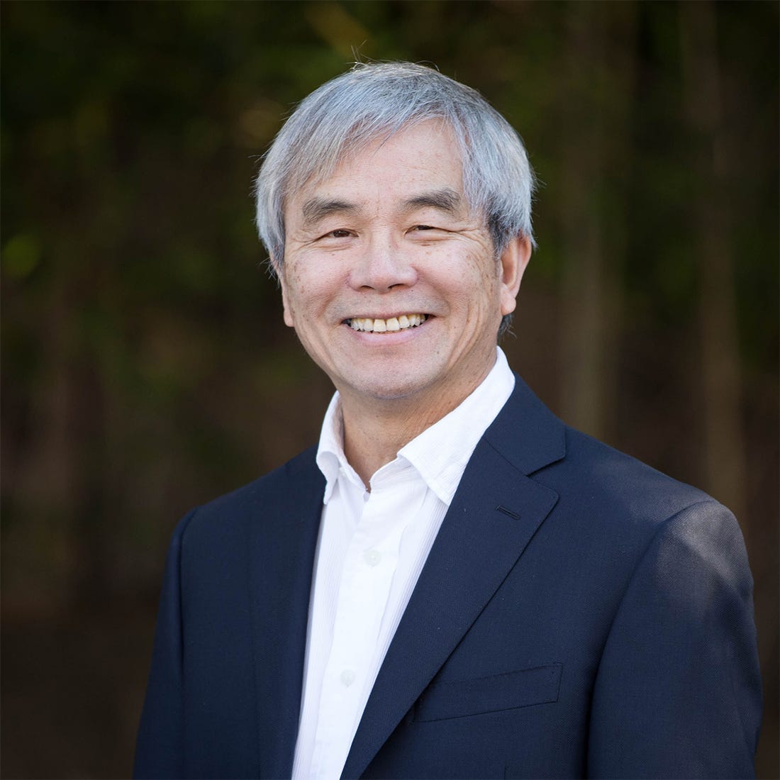Tom Hui smiling outdoors in a navy jacket and white shirt