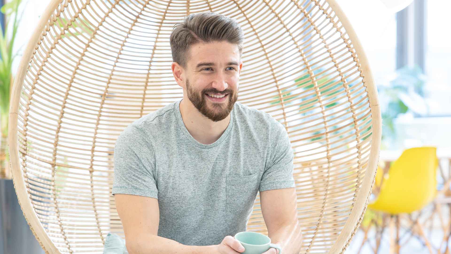 Tom Michels seated in a woven hanging chair, holding a cup