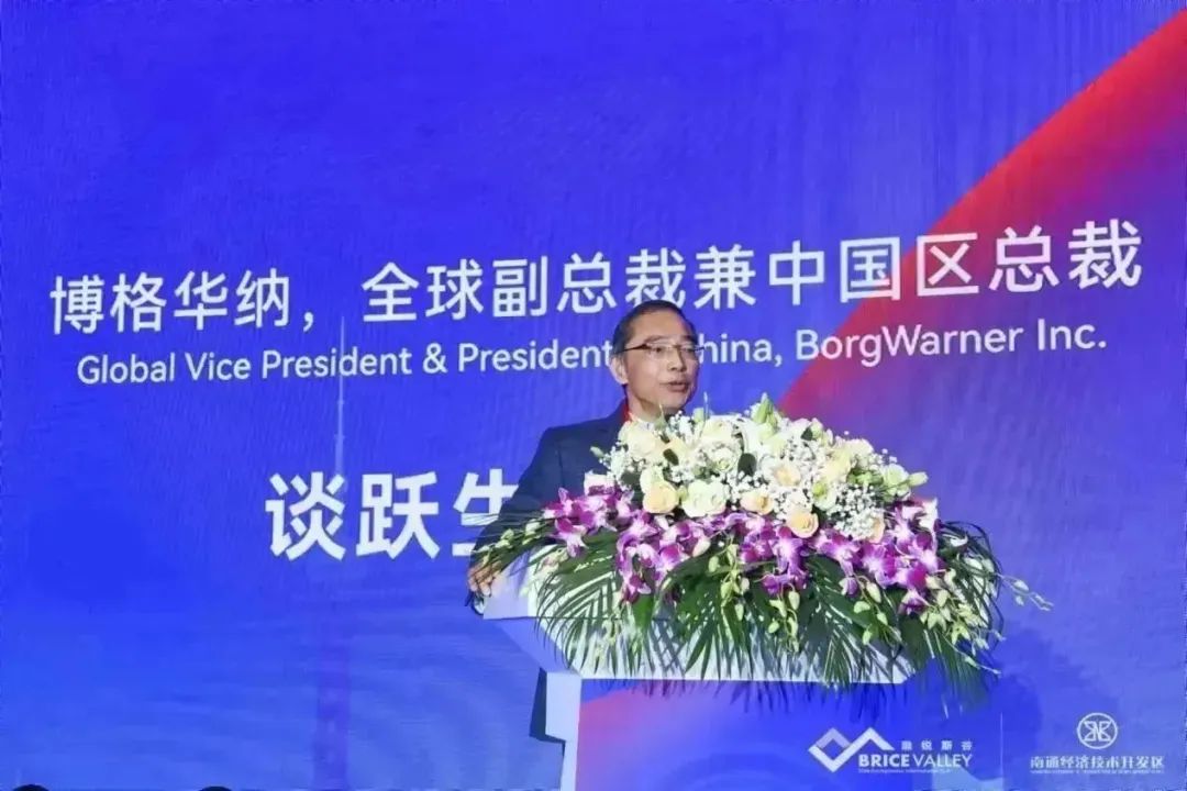 Tom Tan speaking at a forum behind a flower-covered lectern