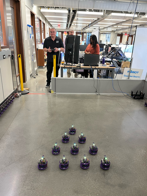 Tom Wagner behind a triangular formation of ten small robots at Northwestern