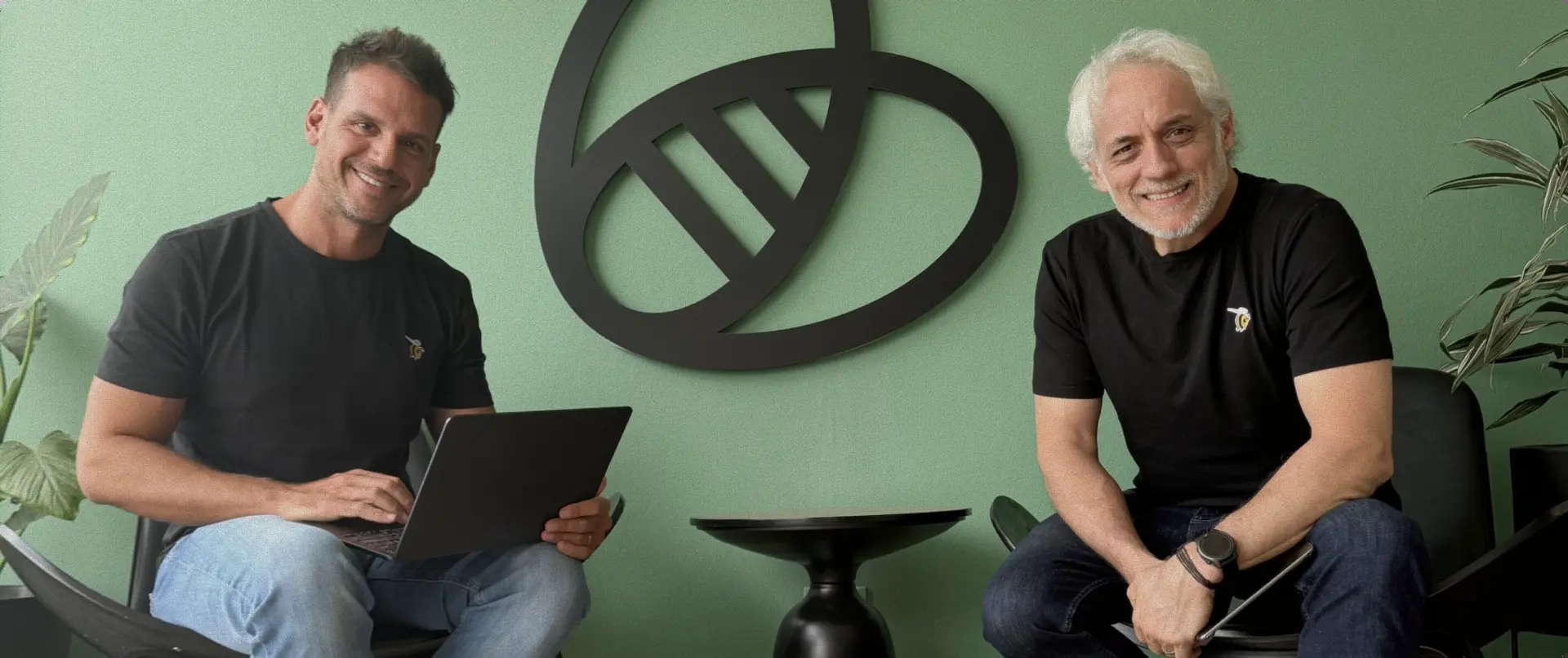 BeeWe co-founders seated with a laptop and tablet beside the company’s bee symbol