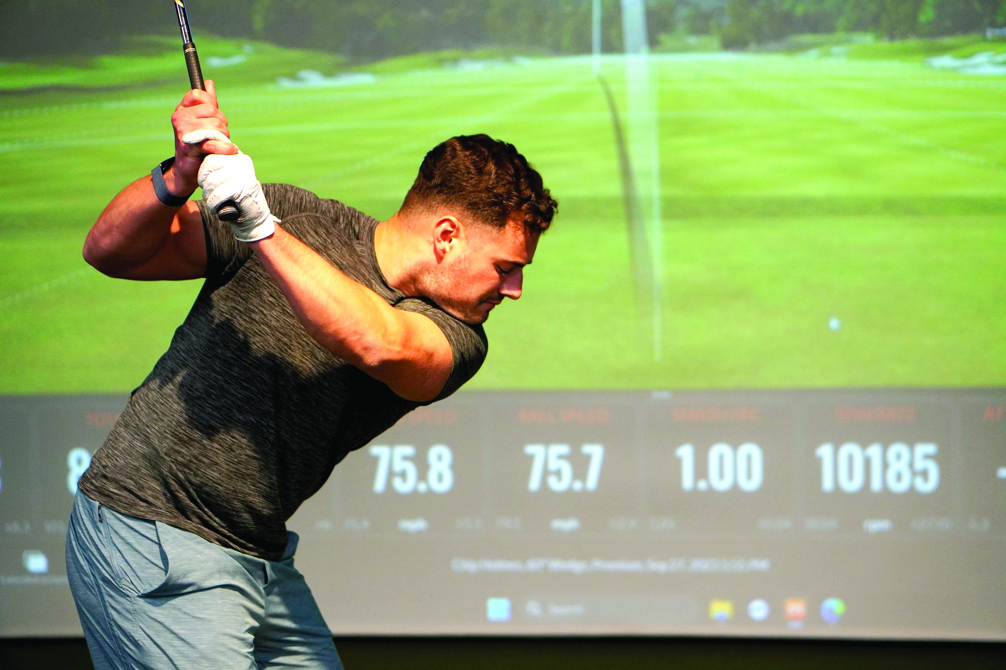 Tommy Graunke practices his golf swing in front of a simulator display