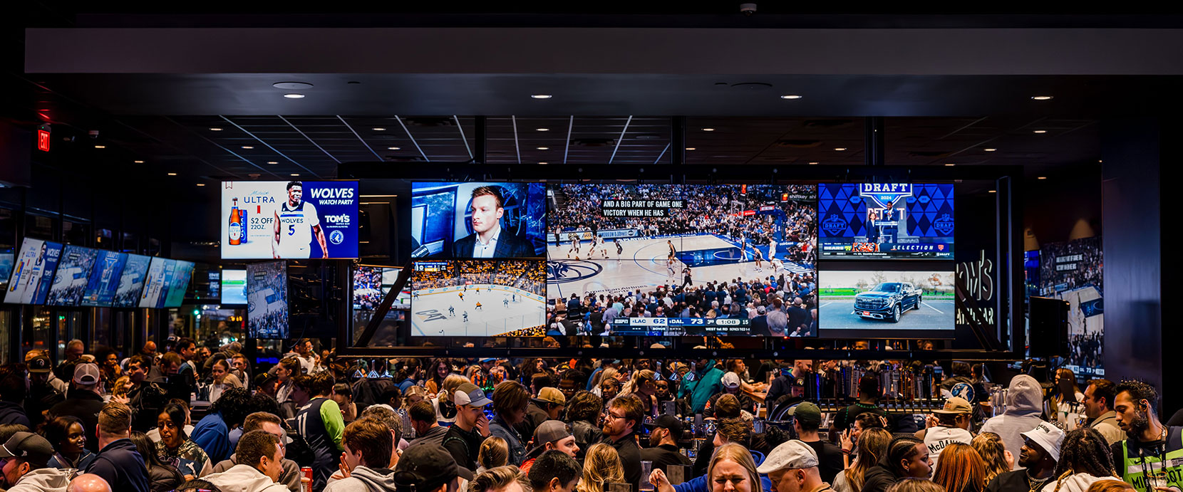 A packed Tom's Watch Bar with a wall of screens showing several games