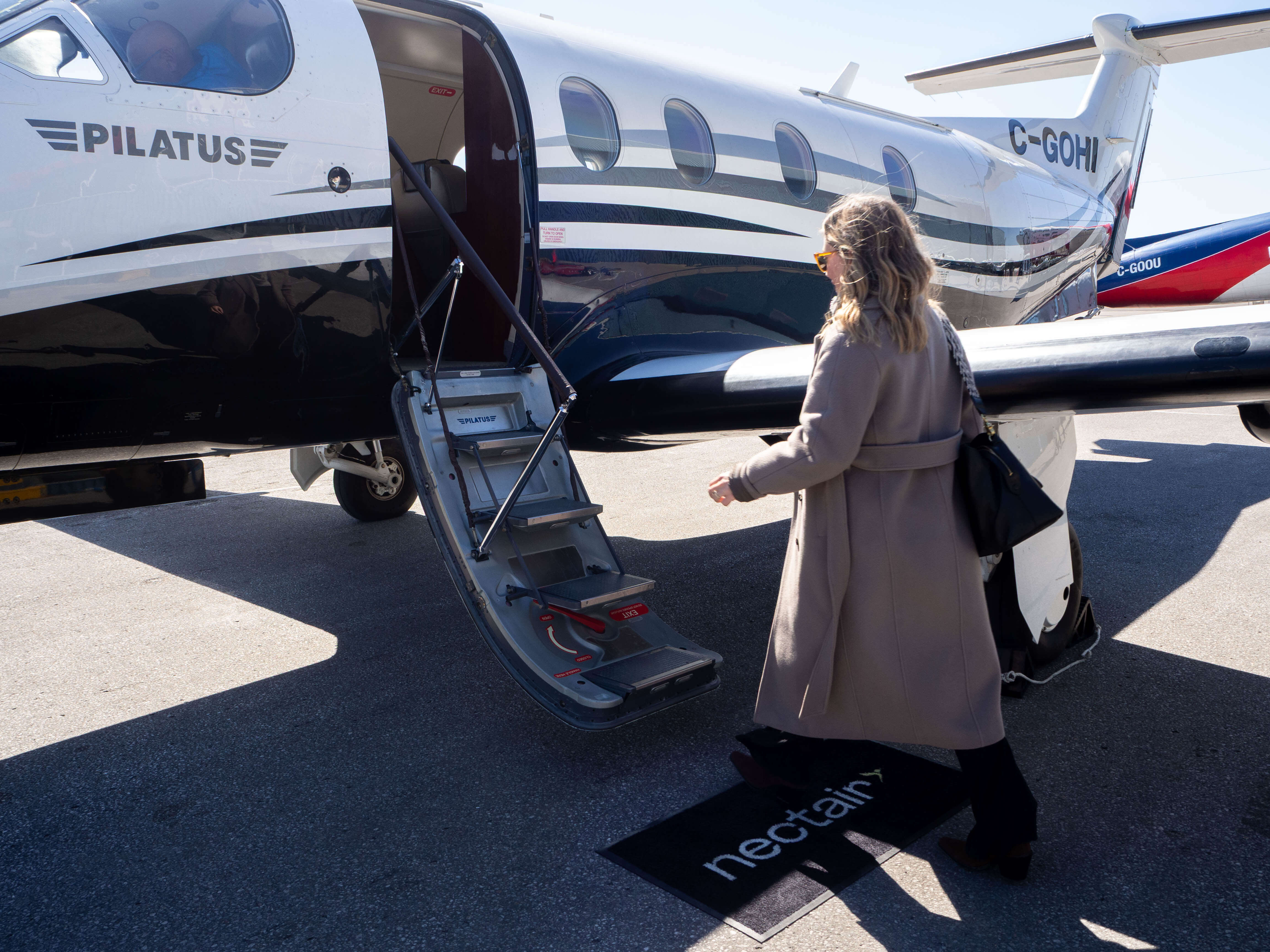 A passenger walks toward the open boarding steps of a NectAir Pilatus aircraft