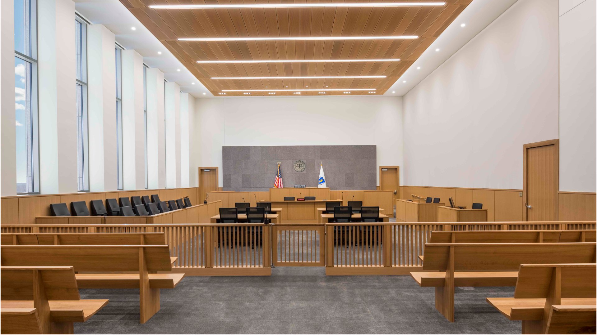 A courtroom with counsel tables, microphones, public seating, and a judge’s bench