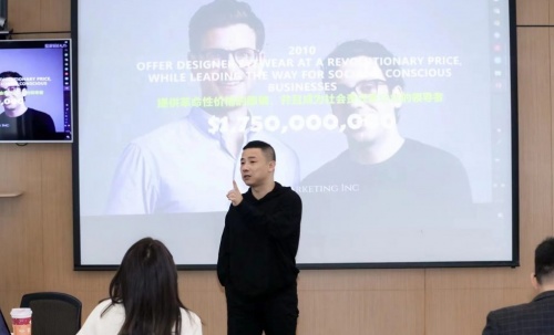 Tony Gu speaking to a seated audience beside a projected brand presentation