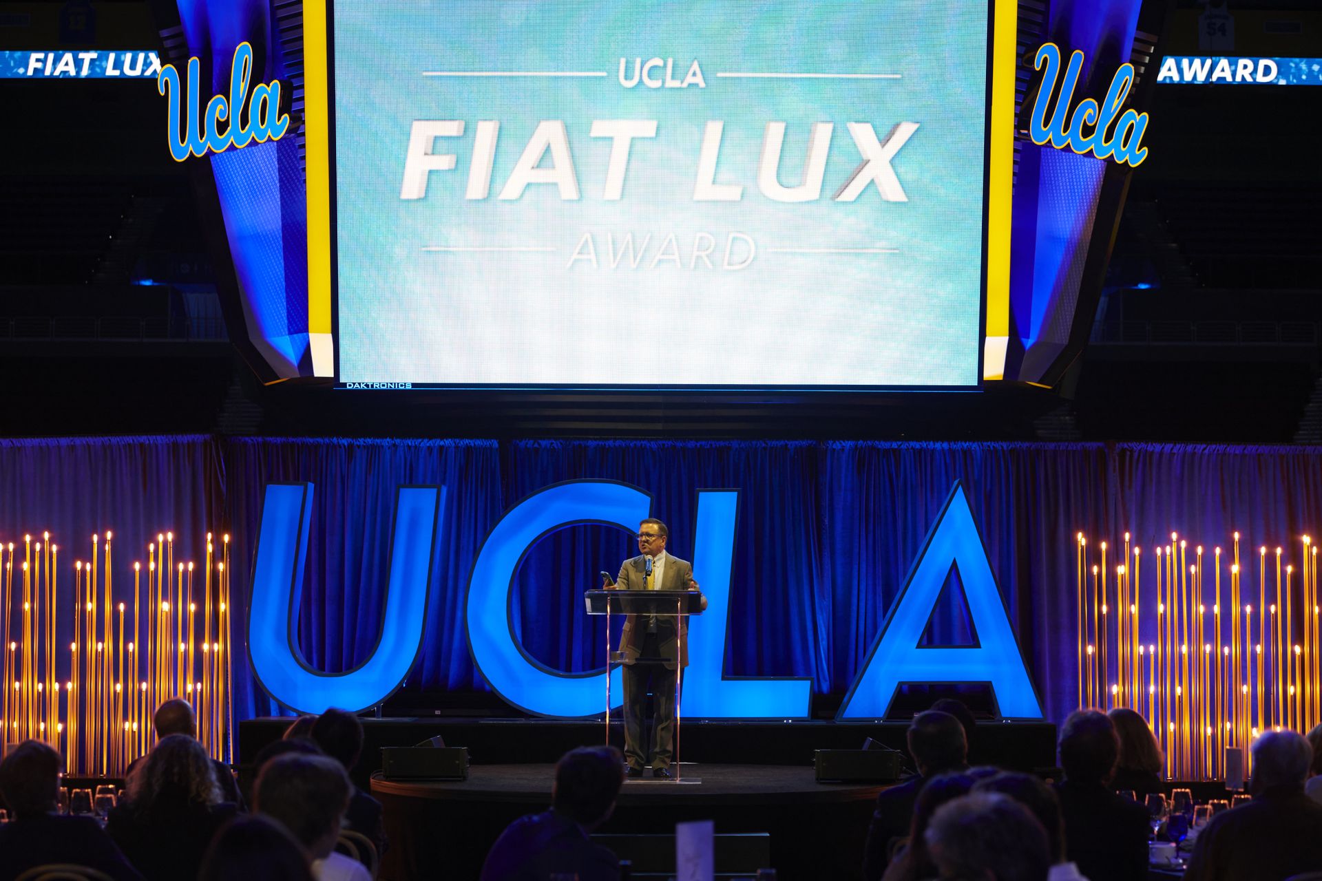 Tony Pritzker speaks at a podium on the UCLA Fiat Lux Award stage in Pauley Pavilion