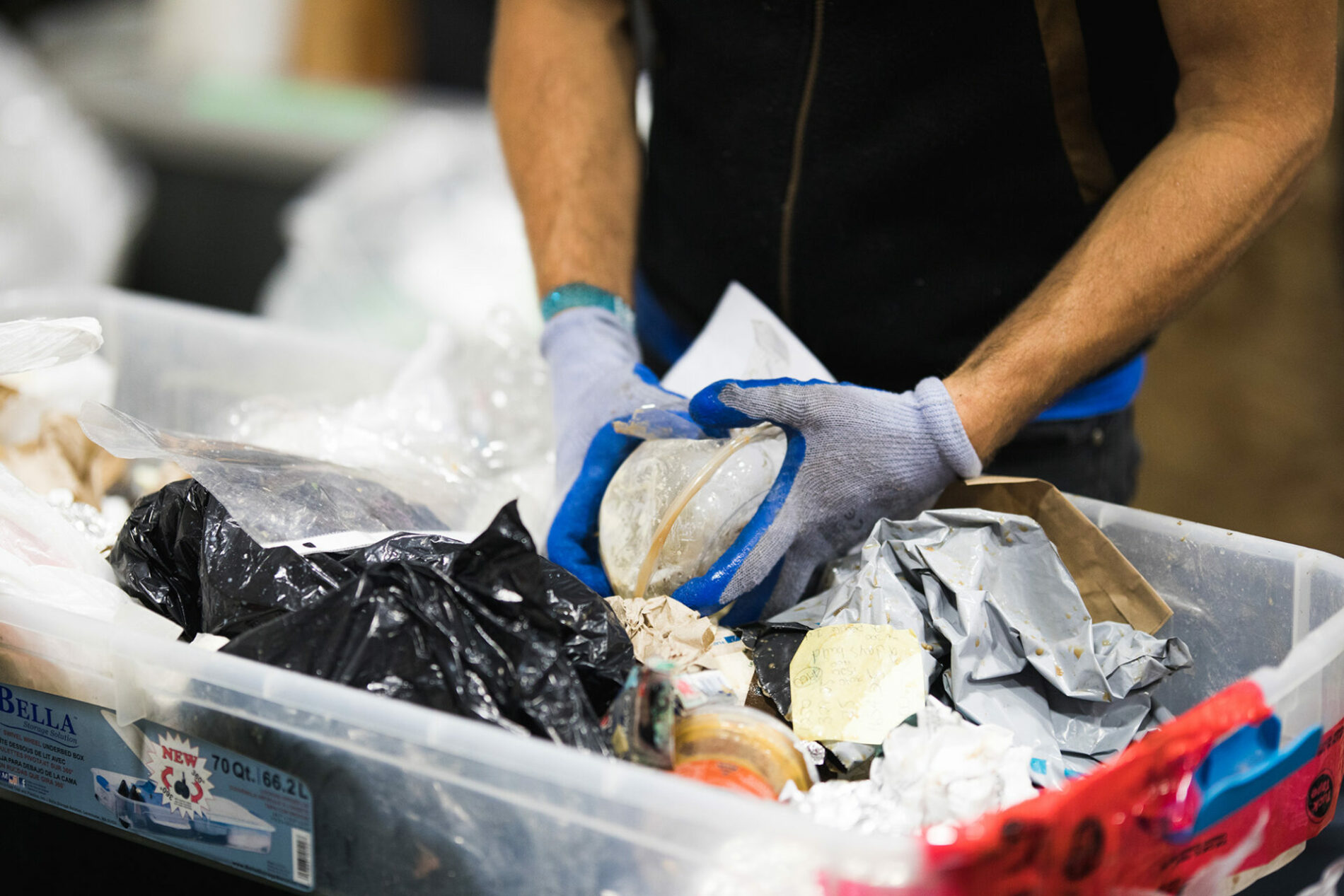 Gloved hands sorting discarded packaging and other waste