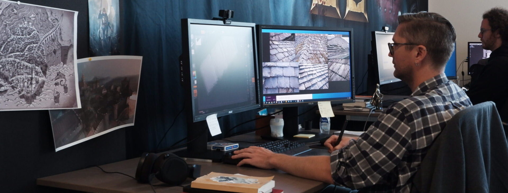 A Torn Banner artist working at a desk with medieval environment references and game textures on screen